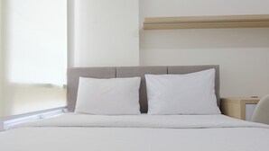 A neatly made bed with white linens and two pillows, a wooden headboard, and a bedside table with a lamp. - Good Deal 1Br Apartment Landmark Residence Bandung (Bandung)