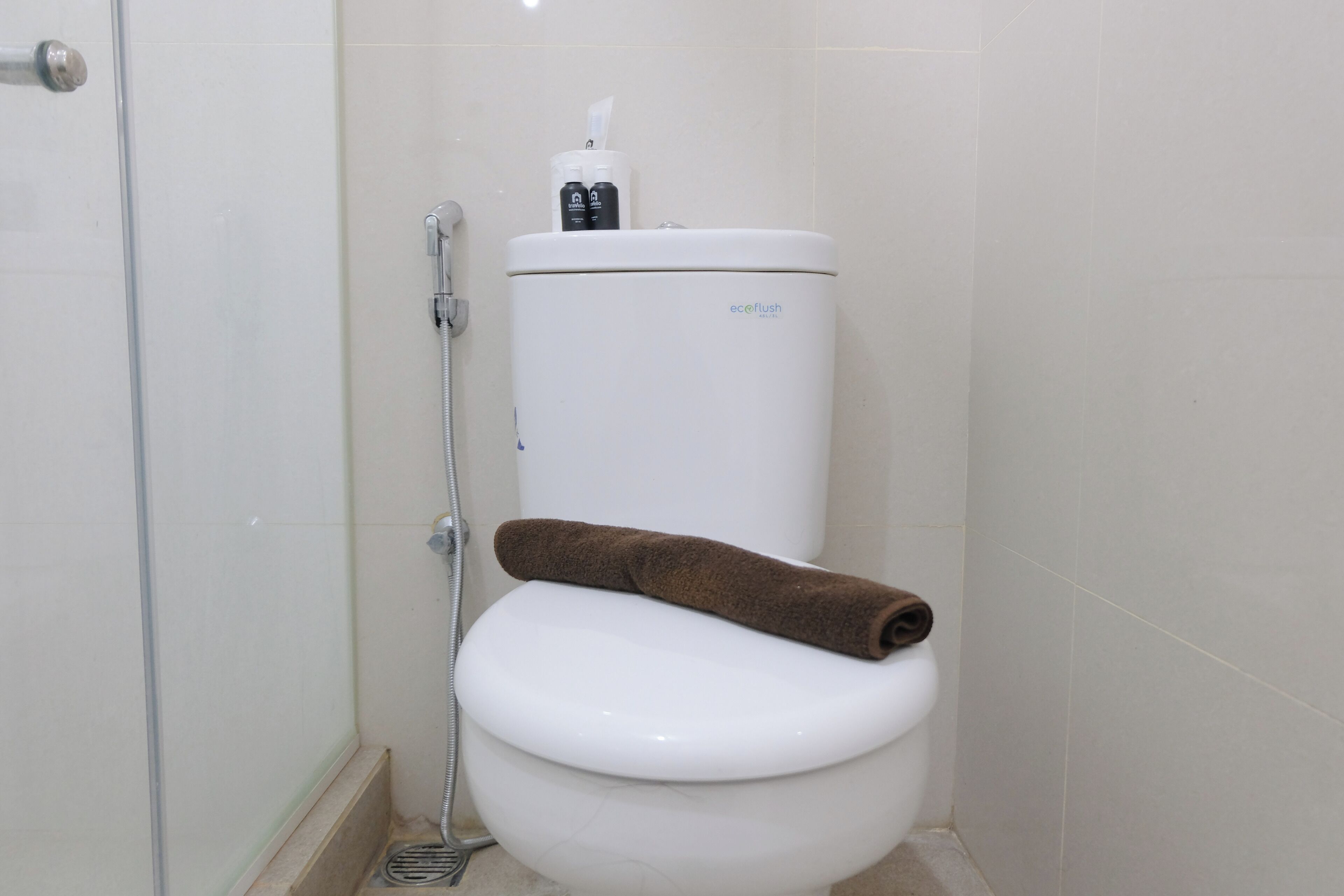 A white toilet with a brown towel on it, a showerhead, and a toilet paper holder.