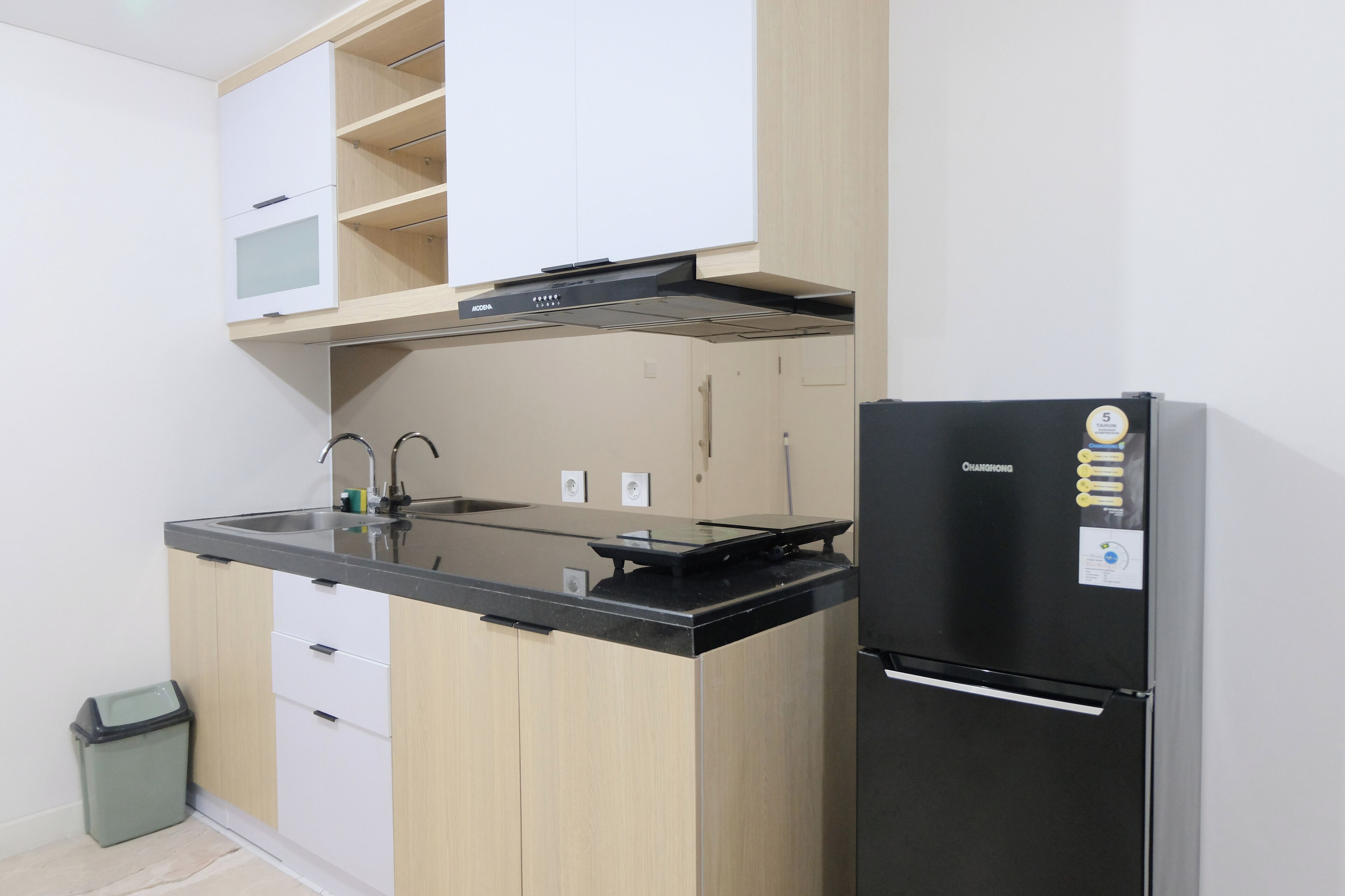 A compact kitchen with a black refrigerator, a sink, and wooden cabinets.