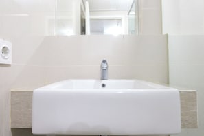 A white bathroom sink with a modern faucet, beige tiles, and a visible electrical outlet on the wall. - Good Deal 1Br Apartment Landmark Residence Bandung (Bandung)