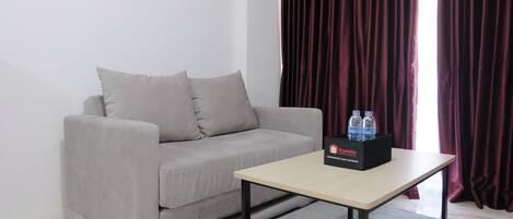 Un salon moderne avec un canapé gris, une petite table et une boîte de bouteilles d’eau.