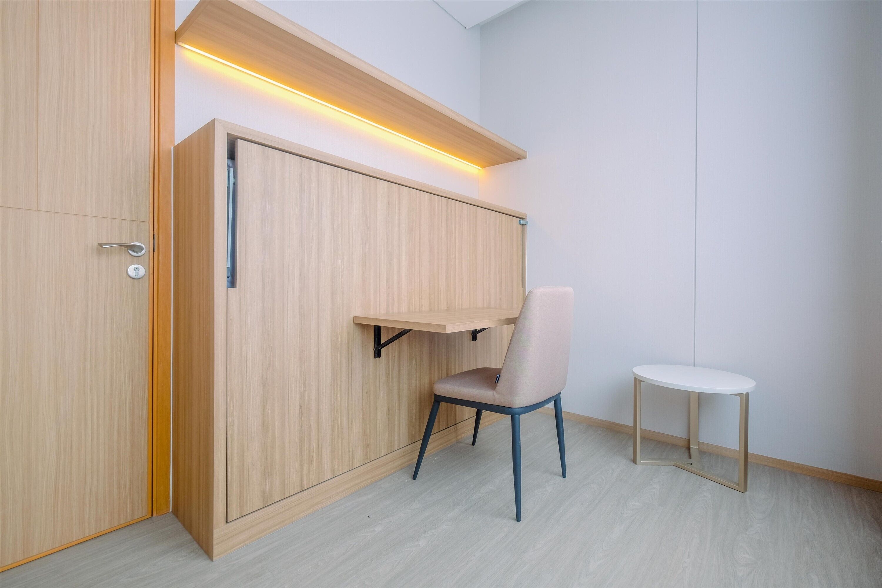 A room with a wooden wardrobe, a chair, and a small table.
