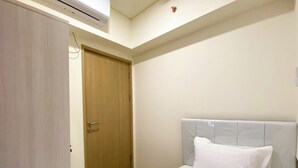 Un dormitorio con puerta de madera, una cama con almohada blanca y un equipo de aire acondicionado en la pared.