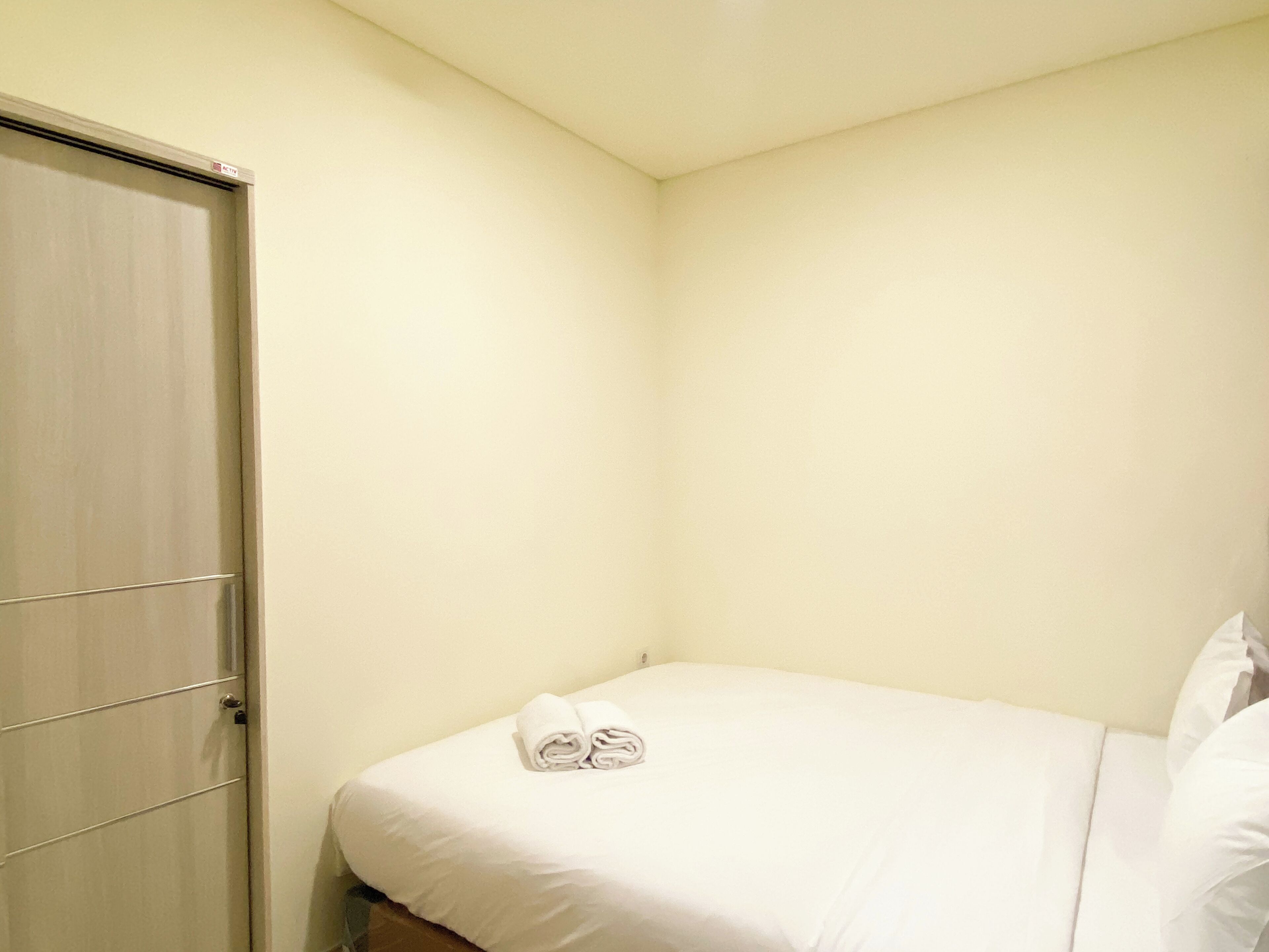 A small, neatly made bed with white bedding and a pair of folded towels on the headboard.