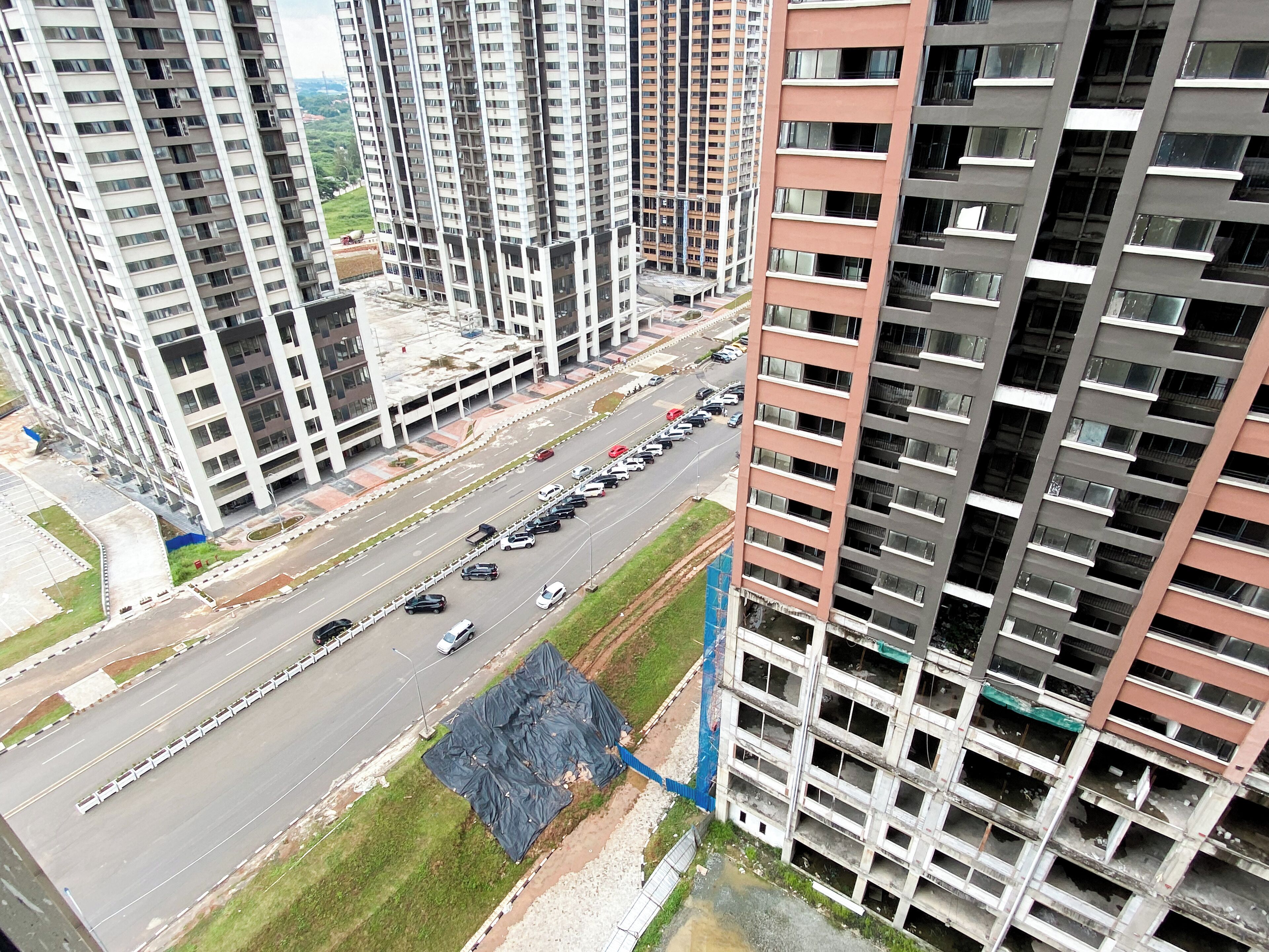 A high-rise building with multiple floors, a parking lot with several cars, and a construction site with exposed concrete and debris.