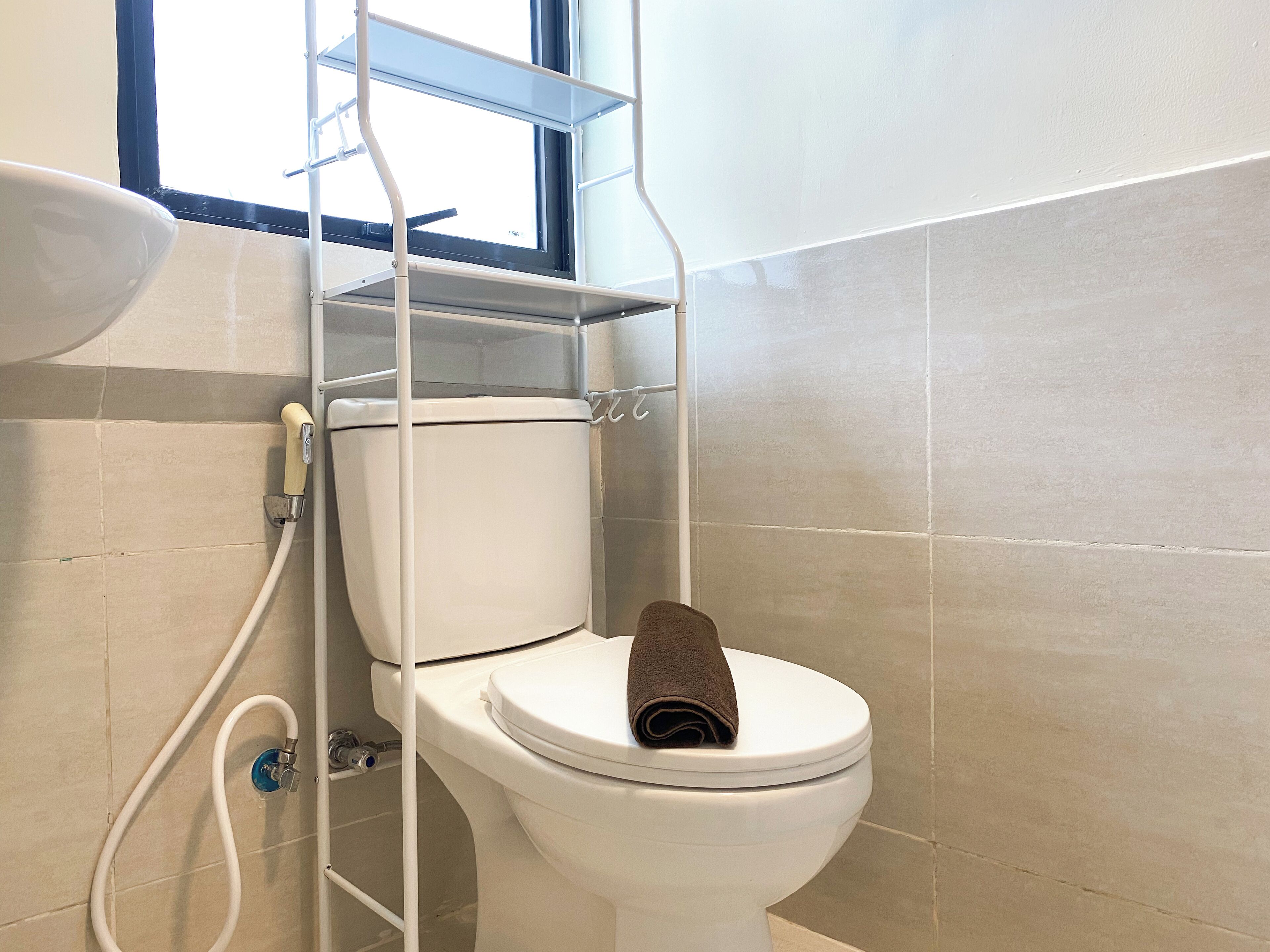 A toilet with a towel on the seat, a window above, and a shower area with a hose.