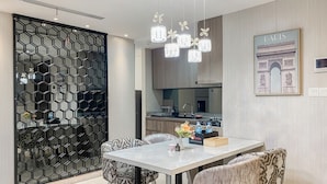 A modern dining area with a white table, patterned chairs, a decorative light fixture, and a kitchen in the background.