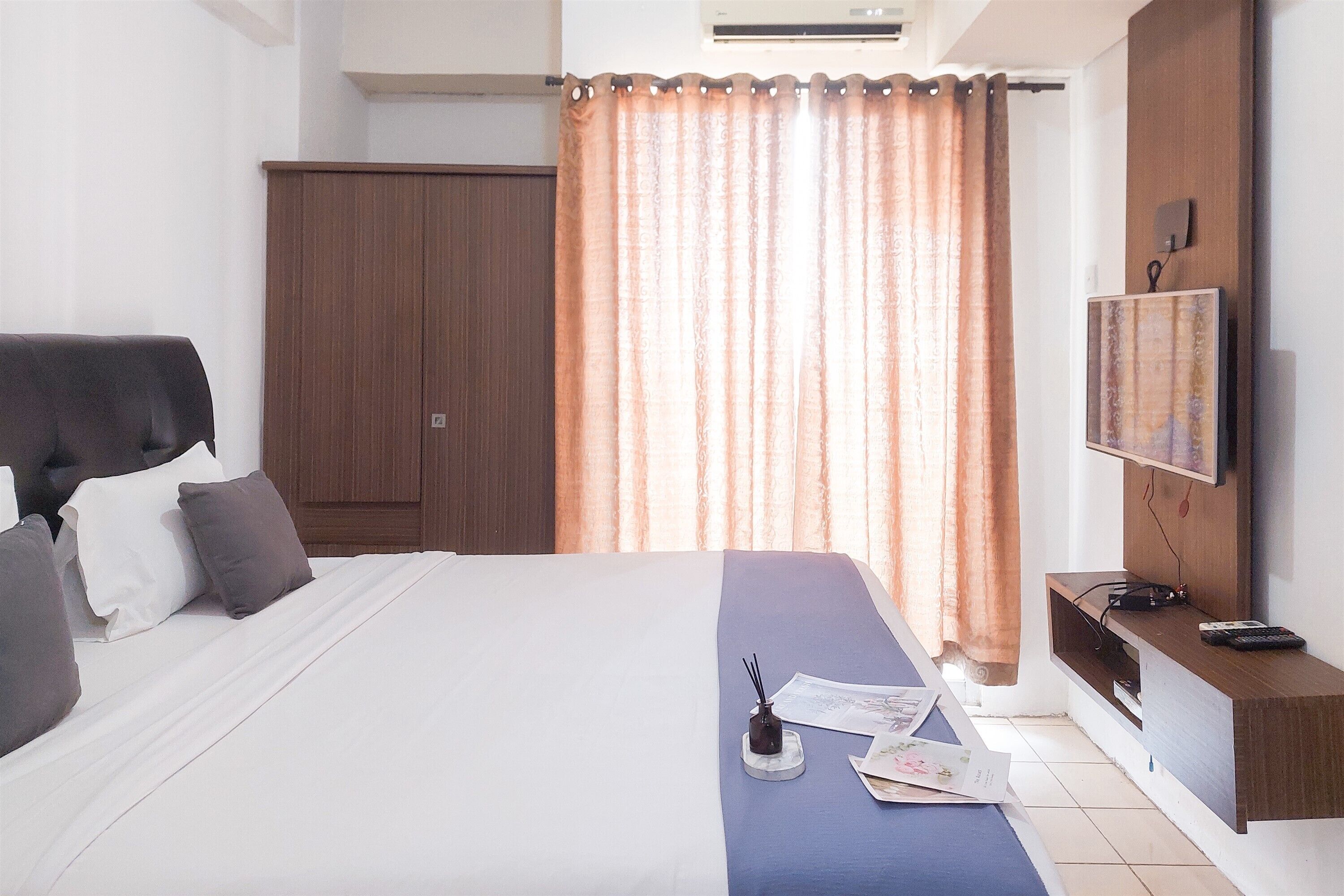 A hotel room with a large bed, a TV mounted on the wall, a wooden wardrobe, and a curtain.