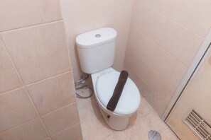 Casa de banho pequena e compacta com sanita branca, cano visível e ventilação na parede.