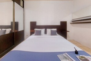 Quarto de hotel com uma cama grande, mesa de cabeceira, espelho e janela.