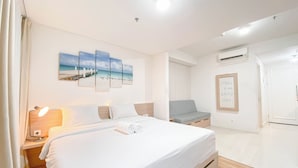 Ein Hotelzimmer mit Bett, Nachttisch mit Lampe, Wand-Klimaanlage, einer Sitzgelegenheit mit Bank und einer gerahmten Botschaft an der Wand.