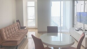 Een moderne woonkamer met een eettafel met glazen blad, een bank en een keukenhoek met een televisie en apparatuur.