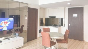 Een moderne keuken met een magnetron, fornuis en gootsteen, een eethoek met een glazen tafel en stoelen, en een televisie op een kast.