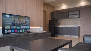 A modern kitchen with a built-in oven and microwave, a dark wooden dining table, and a flat-screen TV mounted on the wall displaying a movie recommendation. - Comfy And Modern Look 2Br At Yukata Suites Apartment (South Tangerang)