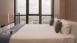 A bedroom with a large window, a bed with white bedding, and a view of a cityscape. - Comfy And Modern Look 2Br At Yukata Suites Apartment (South Tangerang)