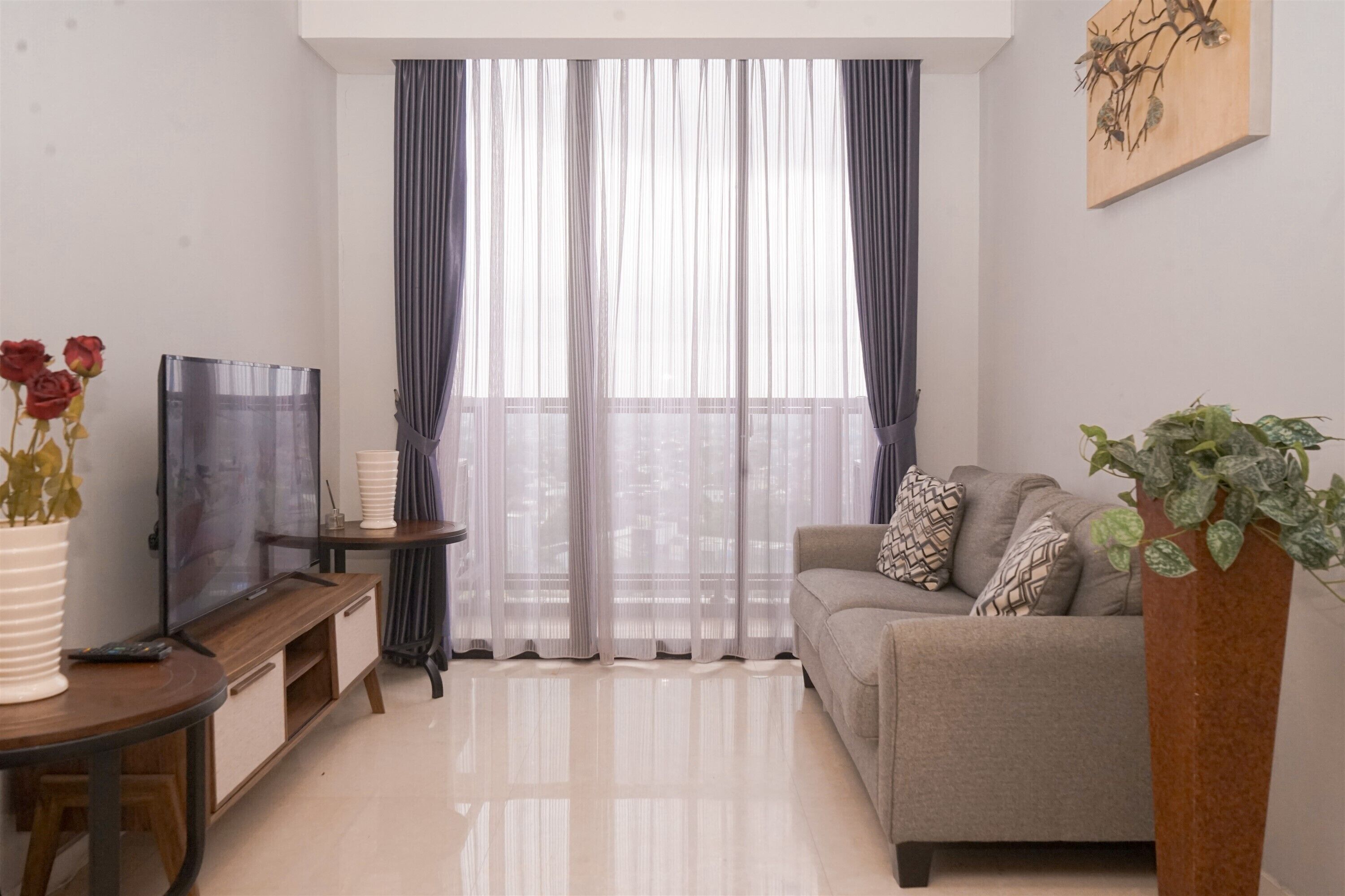A living room with a sofa, a TV on a stand, a plant, and sheer curtains.