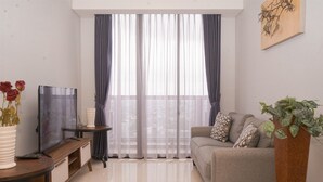 Un soggiorno con divano, televisore su mobile, una pianta e tende leggere.