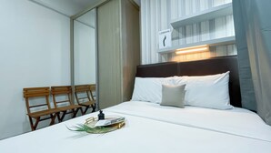 A neatly made bed with white linens, a wooden bench, and a sign indicating the room is in London. - Spacious Studio Apartment B Residence (Pagedangan)