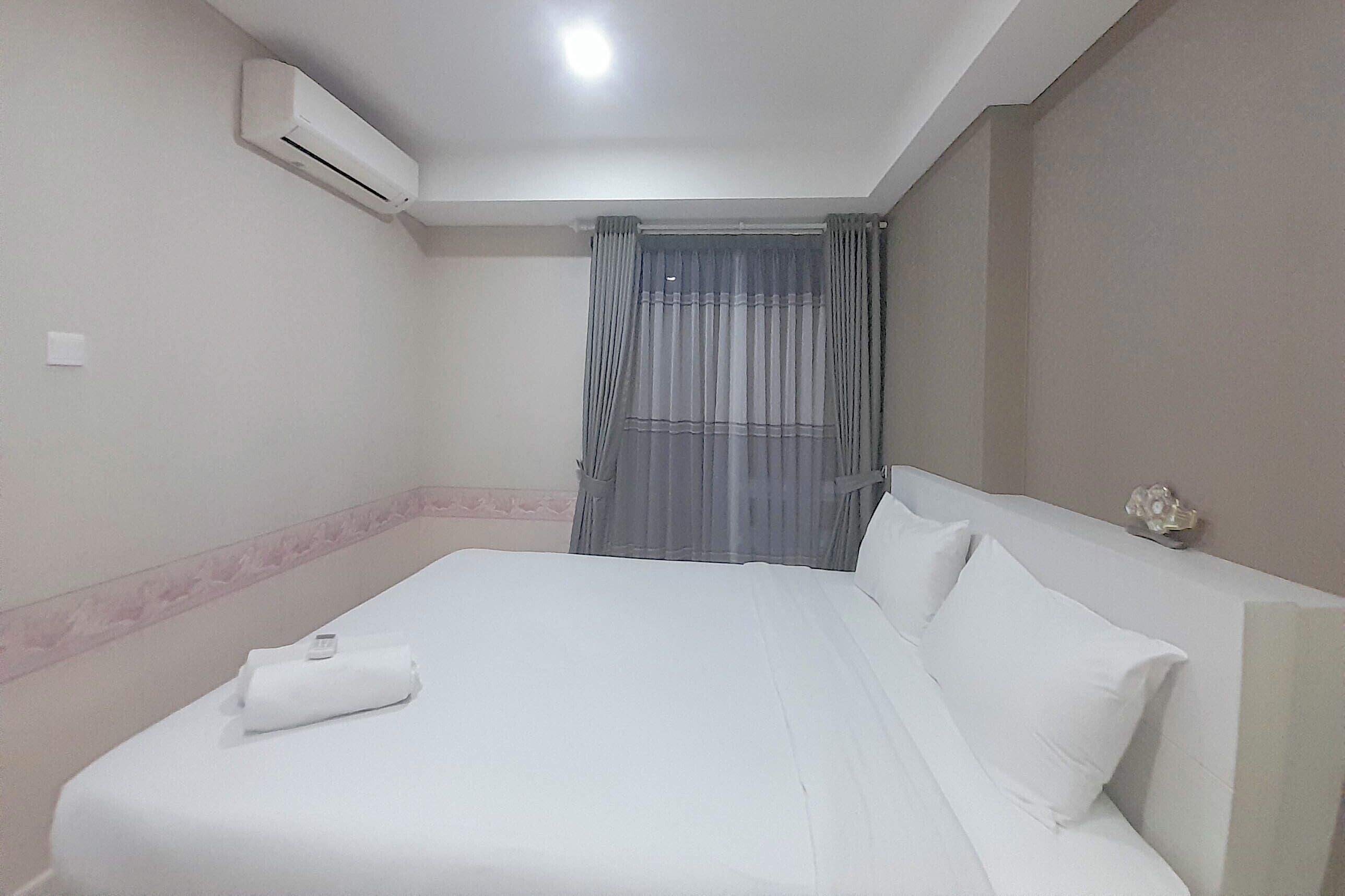 A hotel room with a neatly made bed, an air conditioning unit on the wall, and a window with curtains.