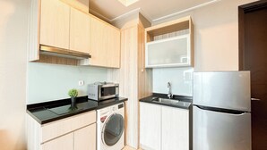 A compact kitchen with wooden cabinets, a washing machine, a microwave, a sink, and a refrigerator. - Comfort Living 2Br At Menteng Park Apartment (Jakarta)