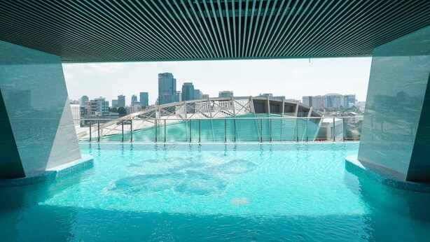 An infinity pool with a city skyline view, a modern bridge, and a clear sky. - Comfort Living 2Br At Menteng Park Apartment (Jakarta)