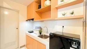 A compact kitchen with wooden cabinets, a built-in dishwasher, a sink, and a small countertop with a kettle and a potted plant. - White Toned Style 2Br Tokyo Riverside Pik 2 Apartment (Teluknaga)