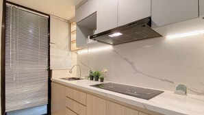 A modern kitchen with a built-in stove, wooden cabinets, and a window with blinds. - Tidy Warm Toned 2Br Apartment Meikarta (Cikarang)