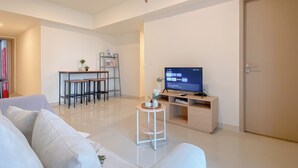 A modern living room with a flat-screen TV, a dining area with a small table and chairs, and a large door. - Tidy Warm Toned 2Br Apartment Meikarta (Cikarang)