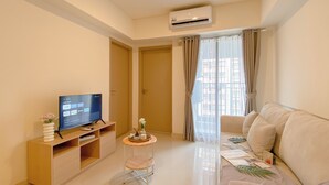 A modern living room with a flat-screen TV, a small round table with a vase, a sofa, and a window with curtains. - Tidy Warm Toned 2Br Apartment Meikarta (Cikarang)