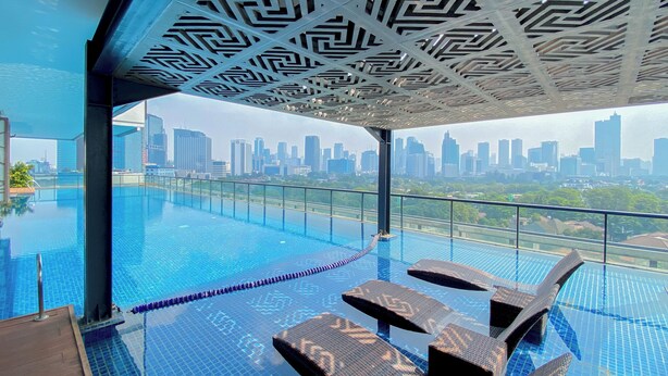 An infinity pool with lounge chairs and a city skyline view. - Modern Furnished 2Br At Samara Suites Apartment (Jakarta)