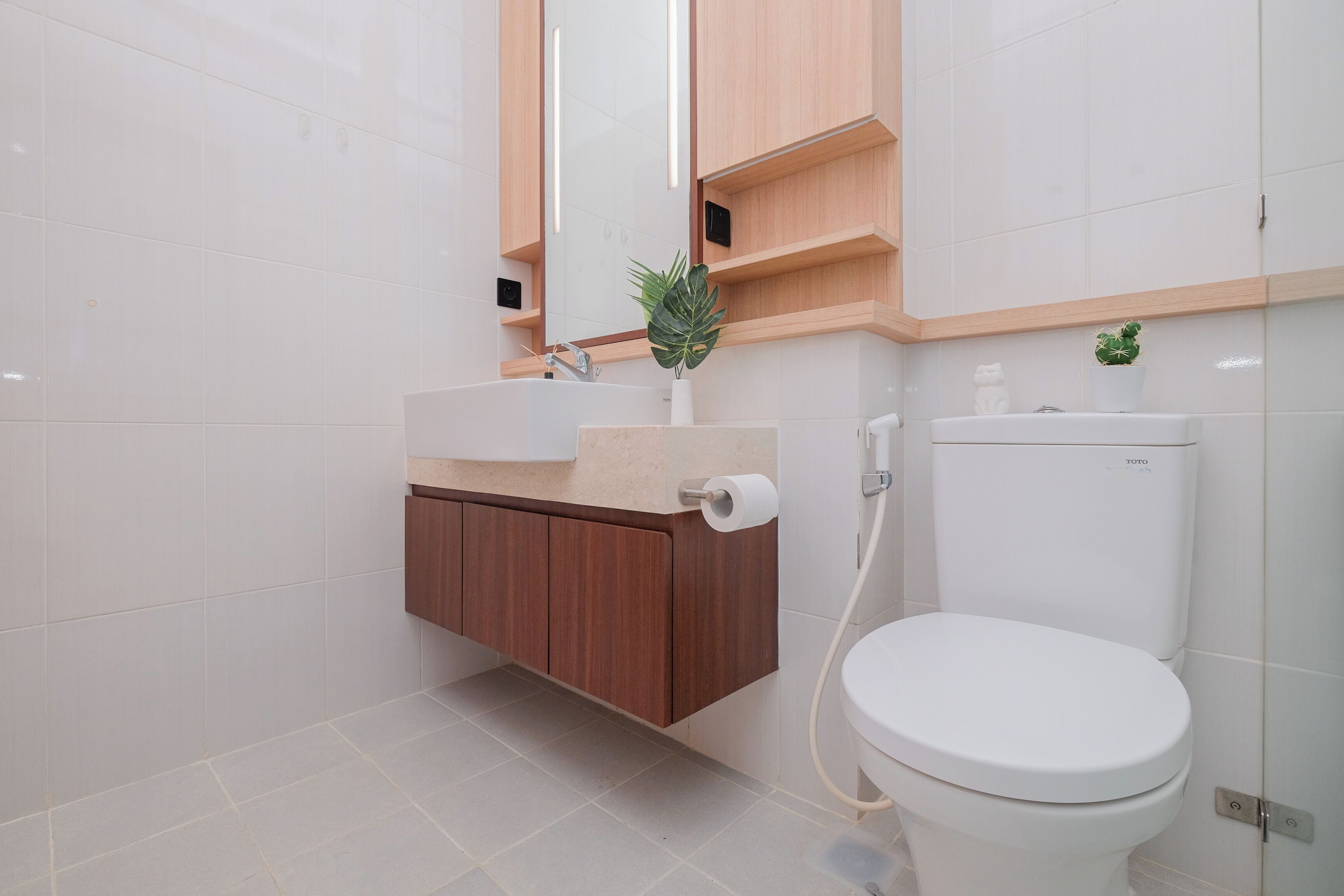 A modern bathroom with a white toilet, a wooden vanity, and a mirror above the sink.