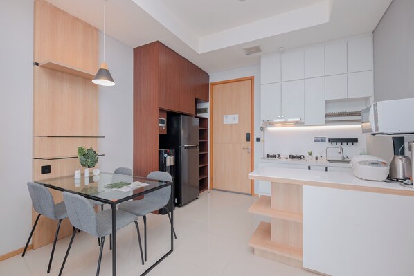 A modern kitchen with a glass dining table, grey chairs, wooden cabinets, and a built-in oven. - Modern Furnished 2Br At Samara Suites Apartment (Jakarta)