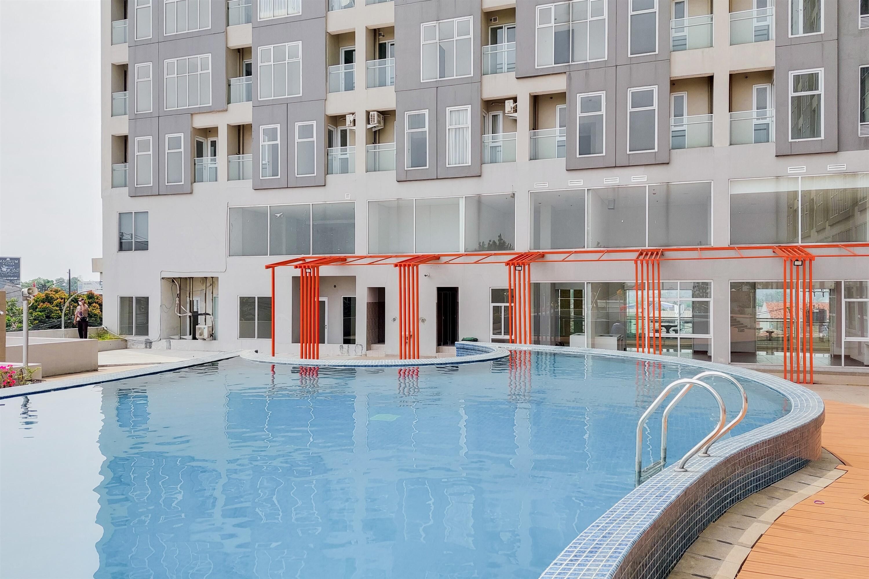 A modern building with a swimming pool, featuring a covered area with red railings and a wooden deck surrounding the pool.