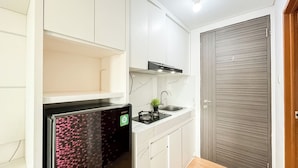 A compact kitchen with white cabinets, a black stove, and a wooden door.
