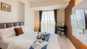 Een hotelkamer met een groot bed, een bureau met stoel, een televisie en een raam met gordijnen.