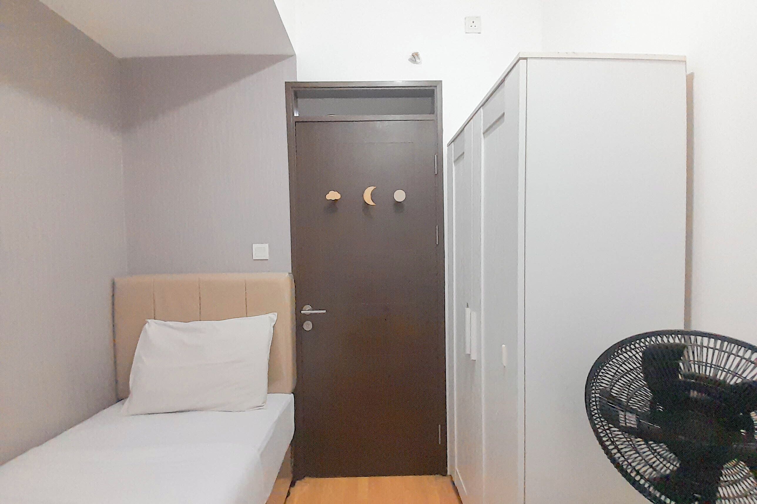 Une petite pièce avec un lit, une armoire et un ventilateur noir.