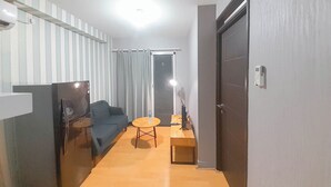 Un espacio habitable pequeño con un sofá, una mesita redonda, un refrigerador y una puerta con interruptor de luz.