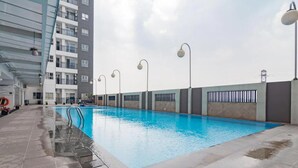Una piscina interior con agua cristalina, rodeada por una terraza con baldosas y un edificio con balcones.