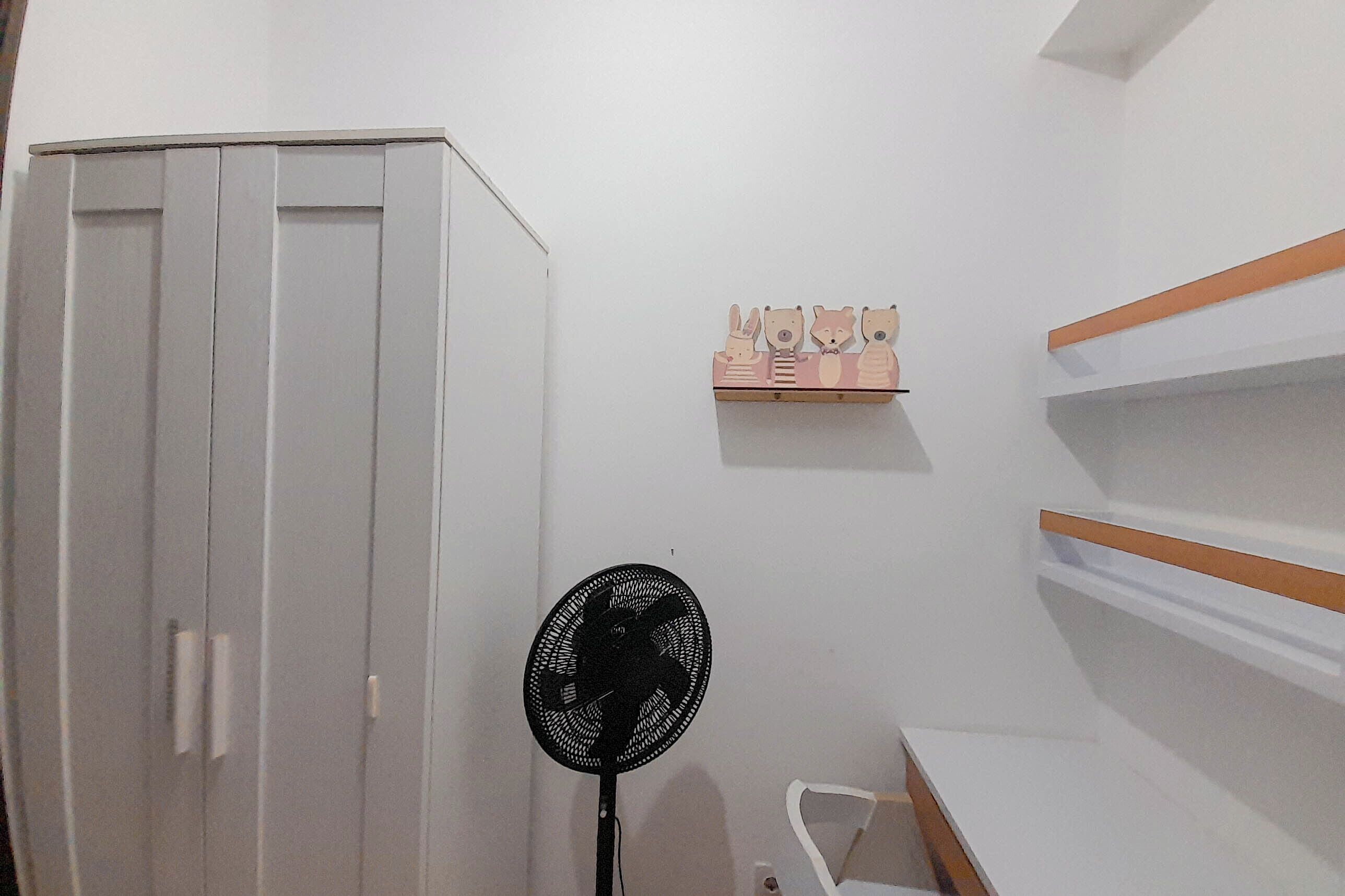 A room with a wardrobe, a fan, and a shelf with wooden animal figures.
