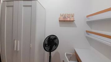 A room with a wardrobe, a fan, and a shelf with wooden animal figures.