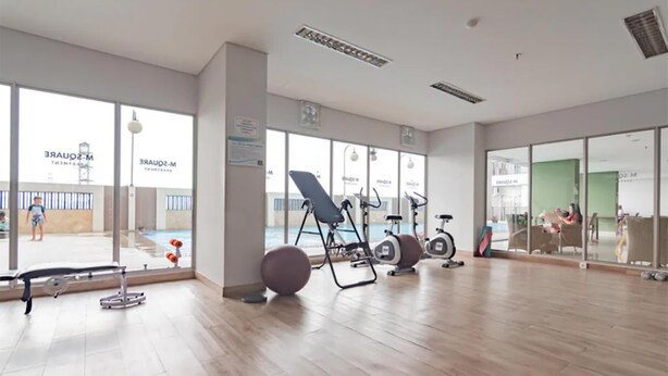 Un gimnasio con equipamiento de ejercicio, amplias ventanas y vistas a una piscina.