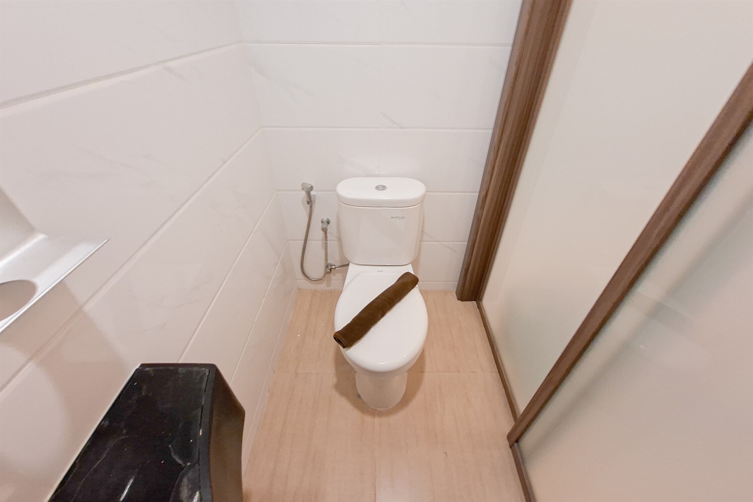A small, narrow bathroom with a white toilet, a shower area, and a wooden bench.