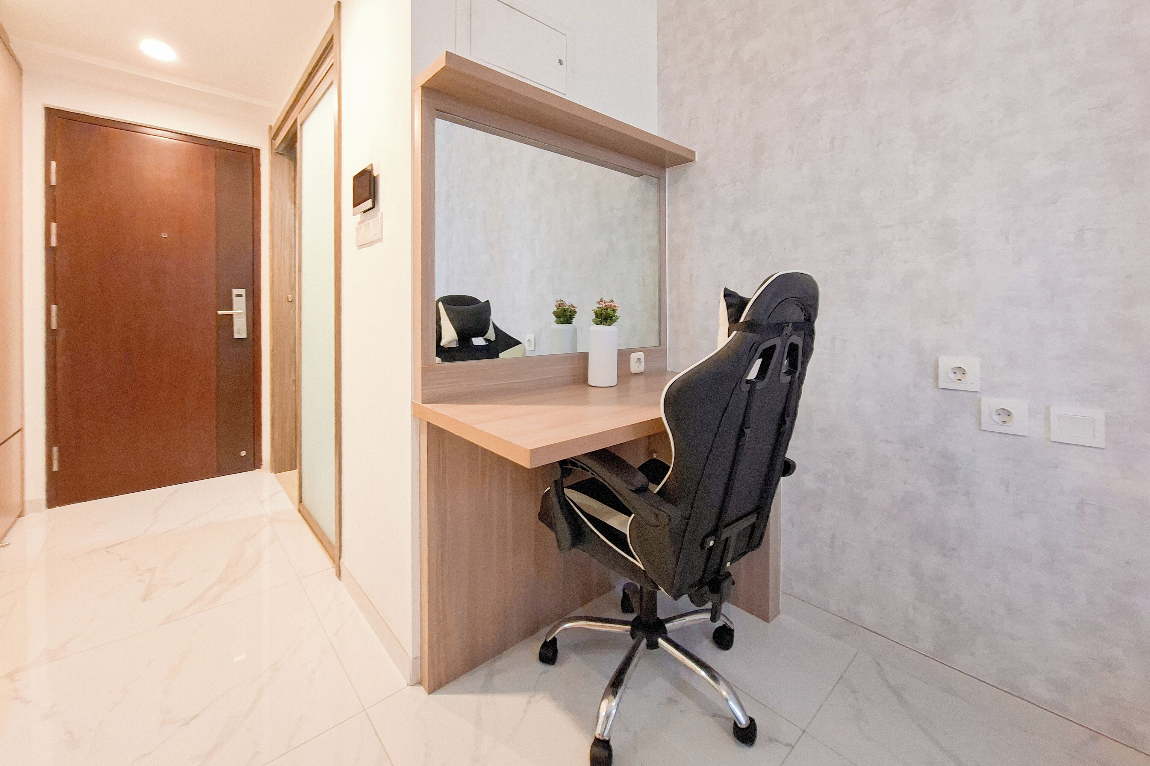 Un espace de bureau moderne avec un bureau en bois, une chaise de bureau noire, un grand miroir et une petite plante en pot.