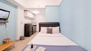 Ein Schlafzimmer mit einem Bett, einem Fernseher, einer Bank und einem kleinen Tisch mit einer Vase und einer Zeitschrift.