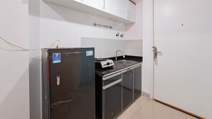 Eine kleine Küche mit einem schwarzen Kühlschrank, einem Herd und einem Spülbecken. Eine weiße Tür und ein weißes Schrank befinden sich über dem Spülbecken.