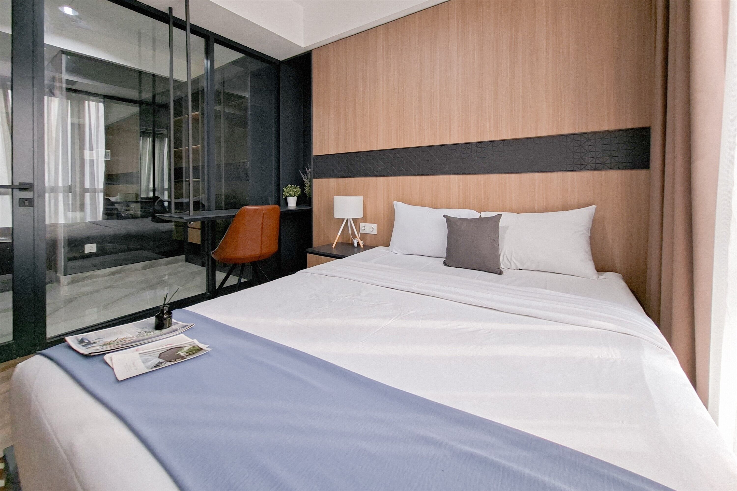 A hotel room with a large bed, a desk with a chair, a lamp, and a view through a glass door.