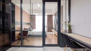 A modern hotel room with a glass door leading to a bedroom, a desk, and a chair. - Modern 1Br Near Ikea At The Smith Alam Sutera Apartment (Tangerang)