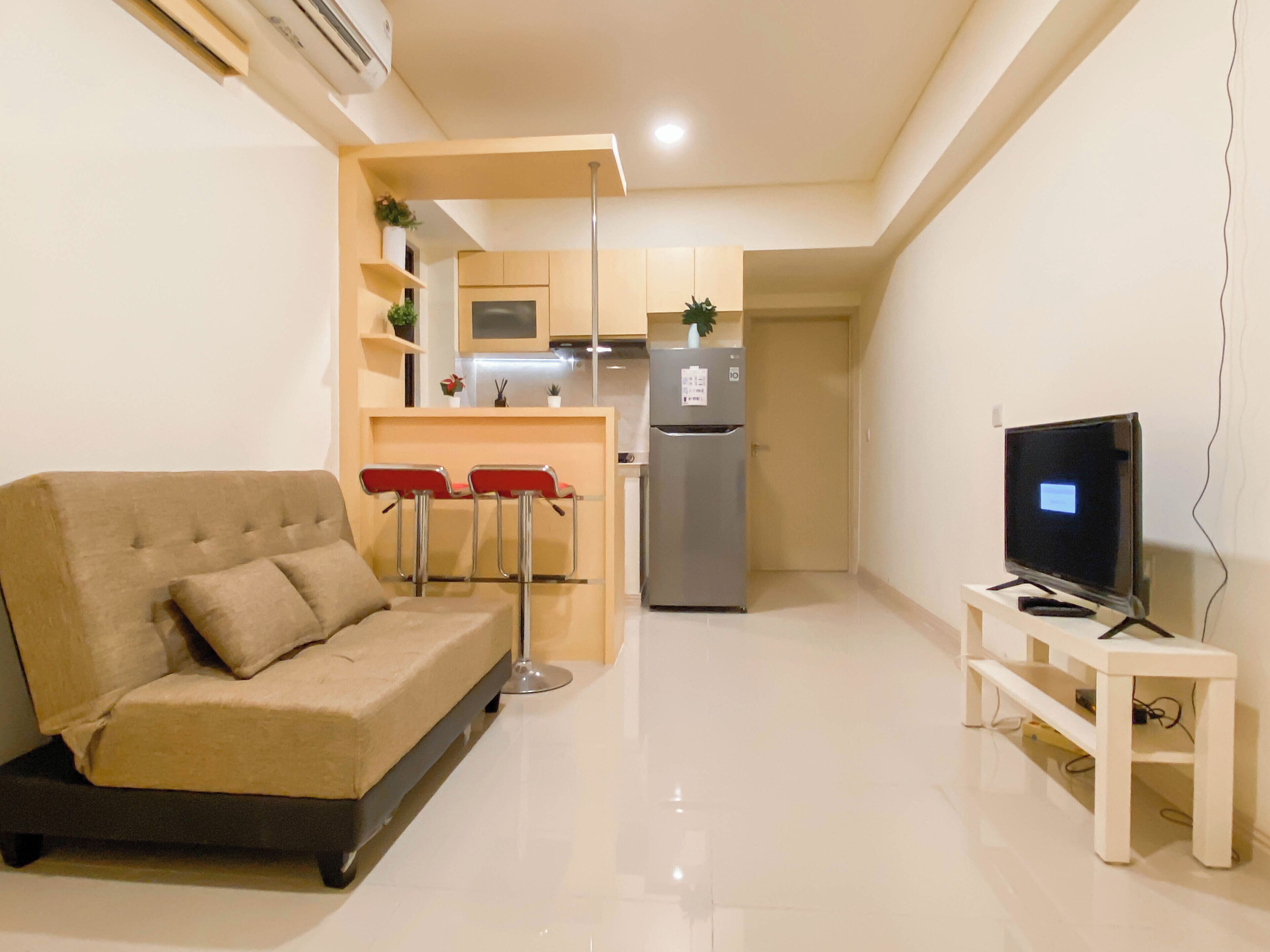 A compact living space with a sofa, a small kitchen area including a refrigerator and microwave, and a television on a stand.
