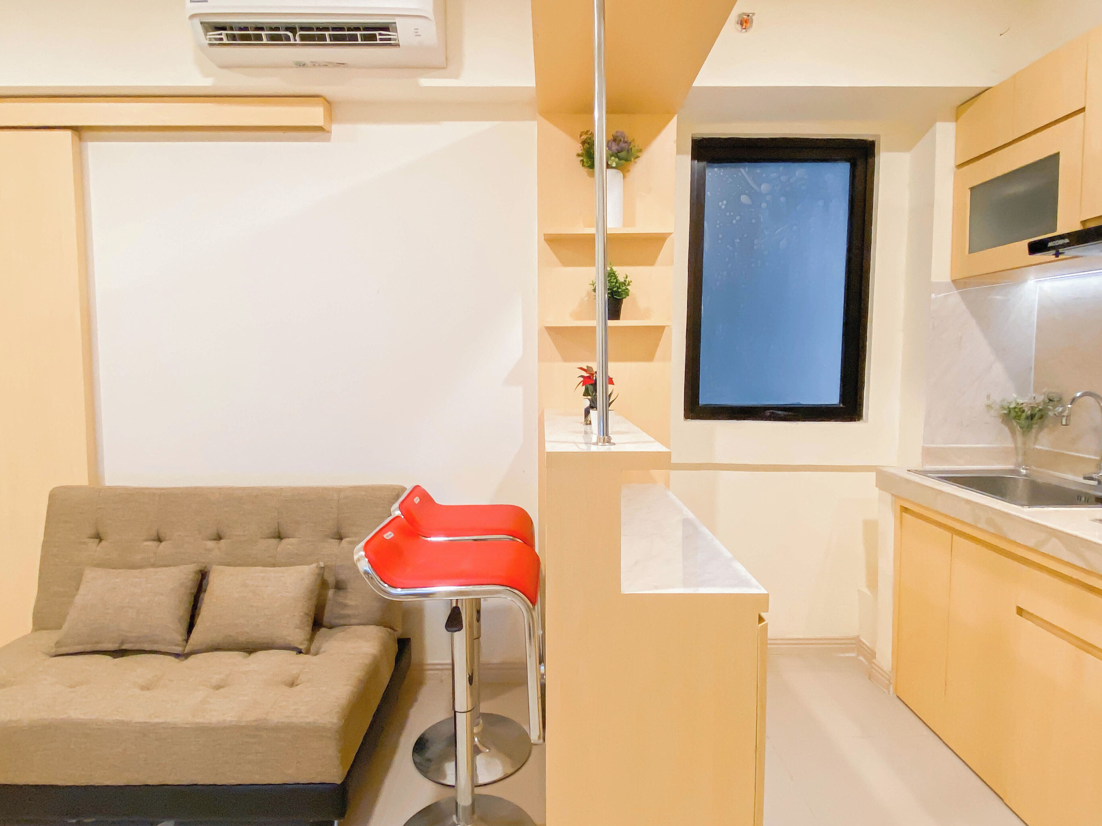 A compact living space with a sofa, a red chair, a kitchen area with a sink, and a window.