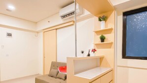 A compact living space with a sofa, a small table, and a shelf with plants. - Modern Contemporary 2Br Apartment At Meikarta (Cikarang)